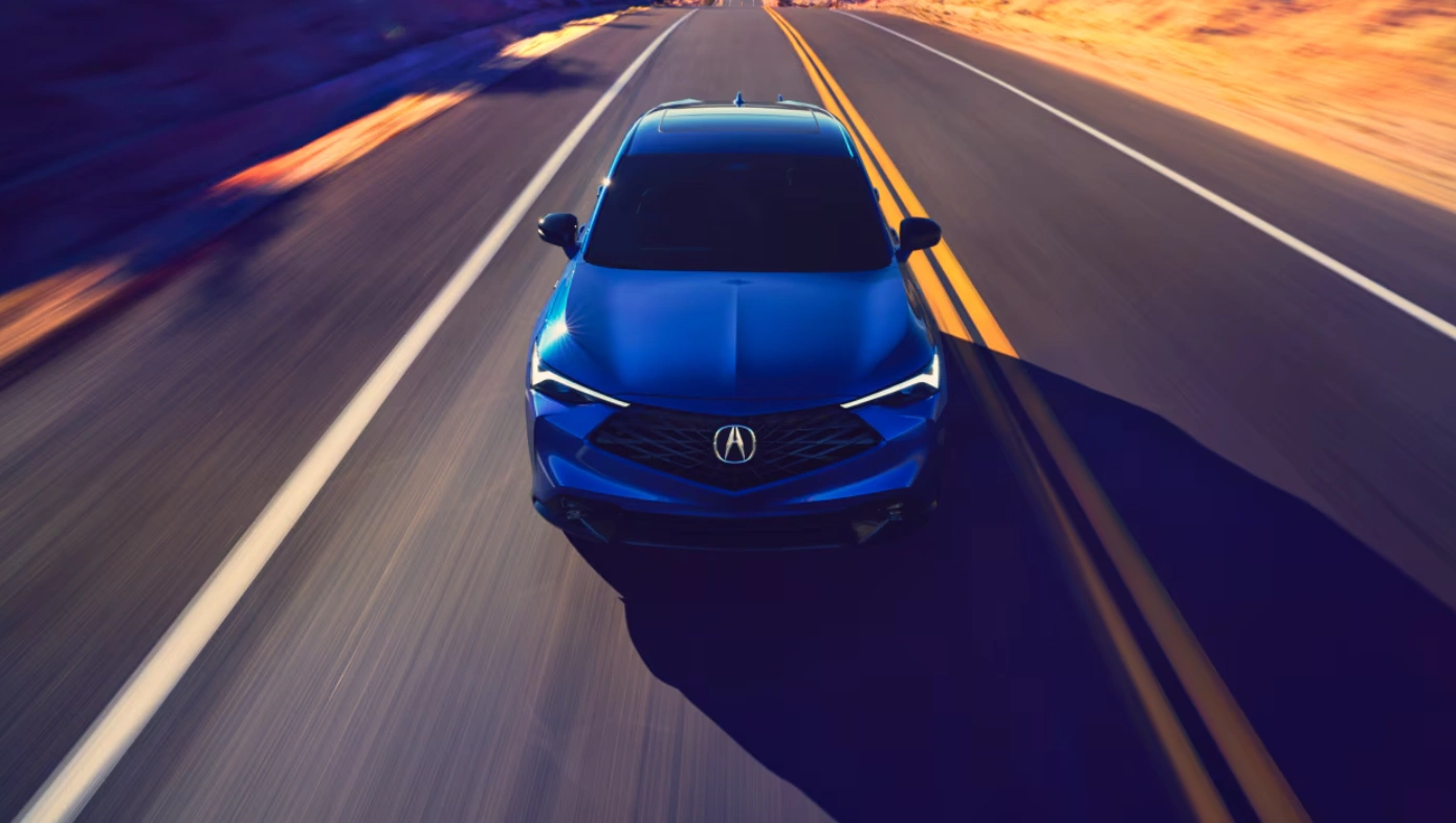 Blue Acura vehicle driving at high speed on a desert road.