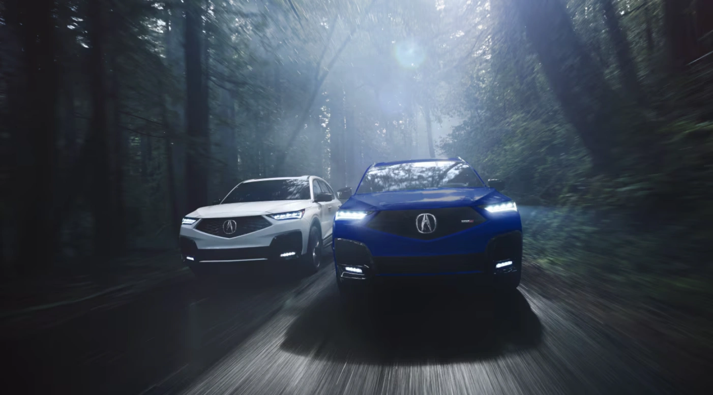 Two Acura SUVs, one white and one blue, driving through a misty forest.