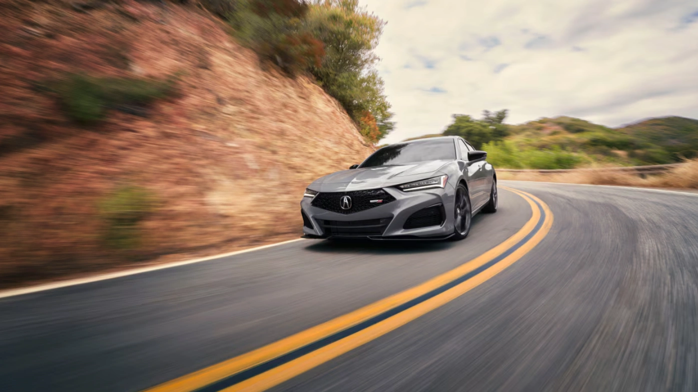 Grey Acura car taking a curve on a mountain road.