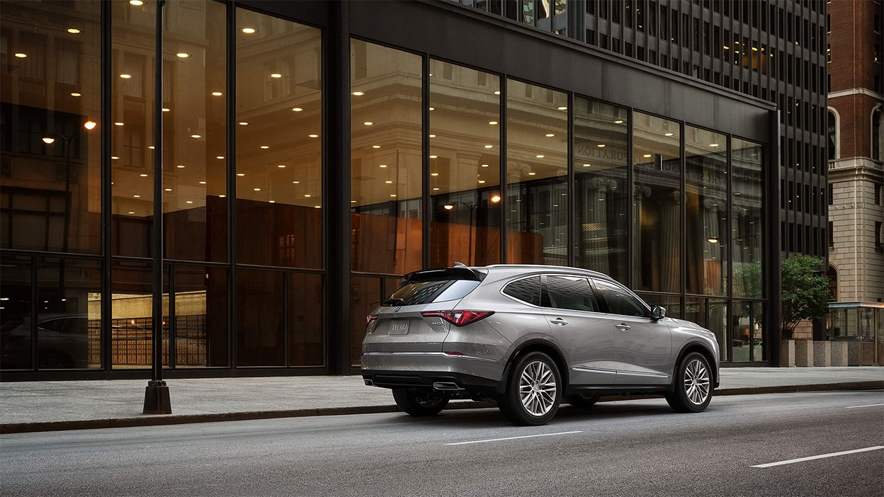 Acura MDX grise 2024 dans les rues d'une ville devant un grand édifice luxueux.